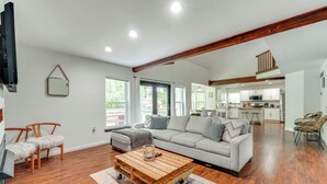 A spacious living area with a large sofa, wooden coffee table, and a kitchen in the background. - Family Home w/ Deck ~ 2 Mi to Camelback Mountain! (Tannersville)
