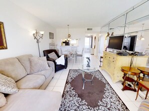 Ein Wohnzimmer mit Sofa, Couchtisch, Fernseher und einem Essbereich mit Stühlen und Tisch.