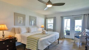 A bedroom with a bed, two bedside lamps, a ceiling fan, a dresser, and a view of the outside through a sliding glass door. - Beachfront on Pass-A-Grille Beach with Pool! Walking Distance to Great Restaurants and Shops. (St. Pete Beach)