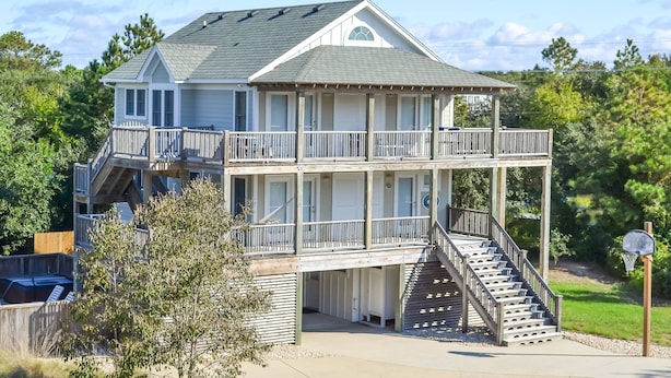 A two-story house with a balcony on the upper floor, a staircase leading to the upper level, and a basketball hoop in the yard. - Duck Haven - Tuckahoe, Easy Walk to Ocean, Pool, Hot Tub, Discounts! (Duck)