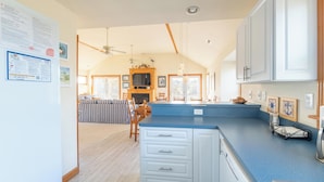 A spacious kitchen with white cabinets, a blue countertop, and a dining area with striped furniture. - Duck Haven - Tuckahoe, Easy Walk to Ocean, Pool, Hot Tub, Discounts! (Duck)
