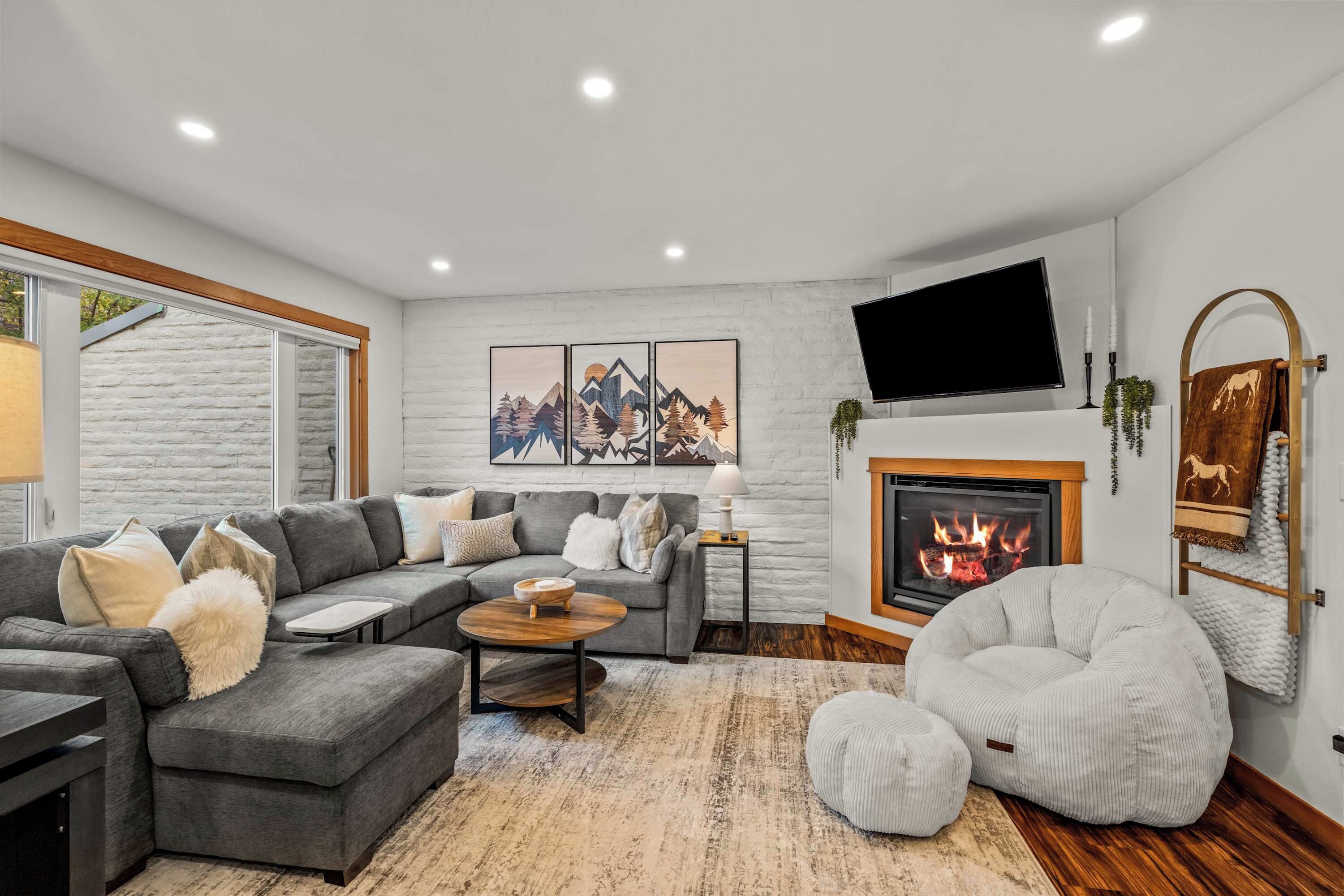 A modern living room with a sectional sofa, a fireplace, a flat-screen TV, and a large window.