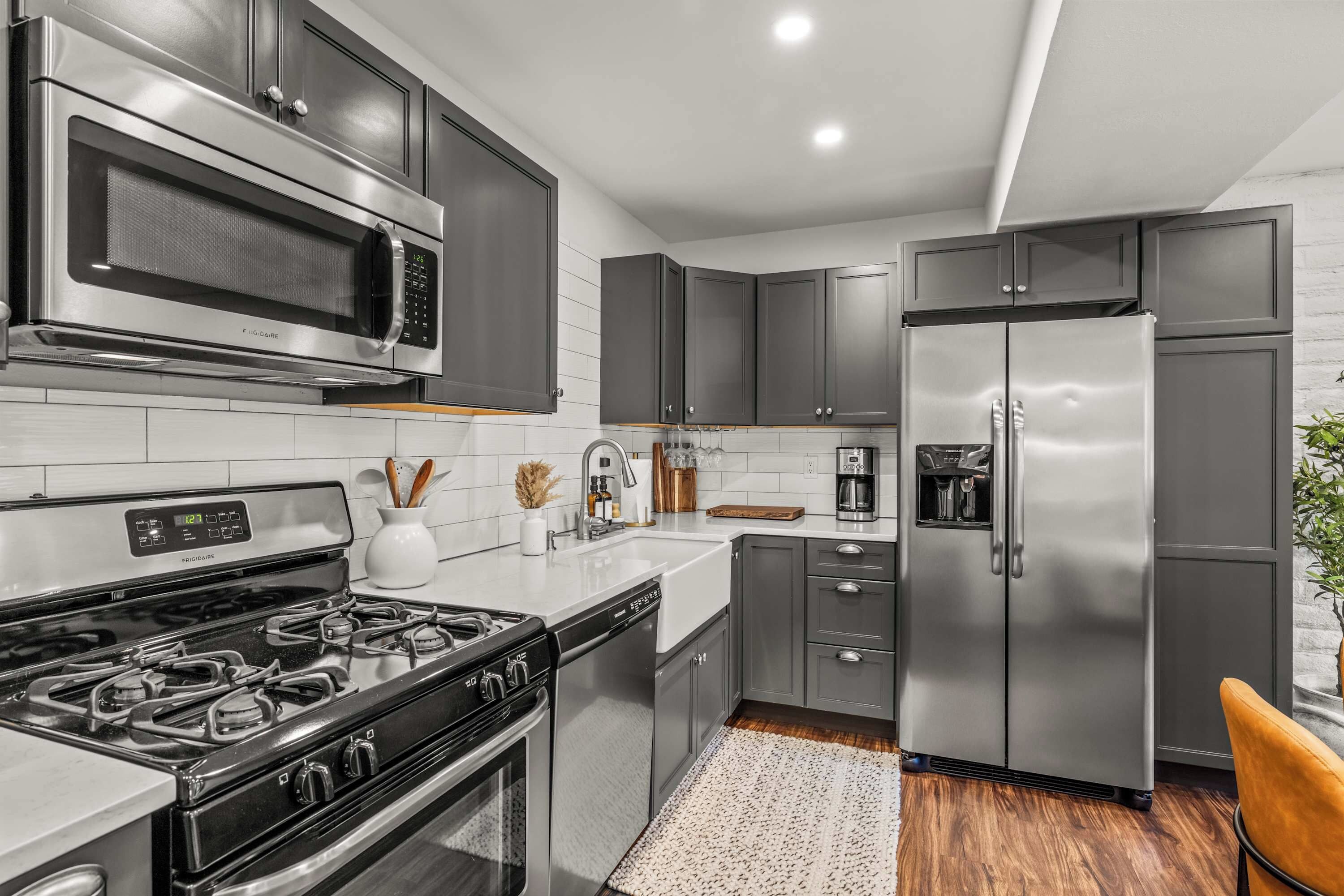 Una cocina moderna con electrodomésticos de acero inoxidable, salpicadero de azulejos blancos y piso de madera.