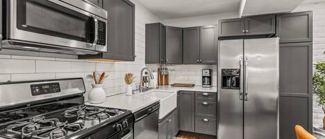 Una cocina moderna con electrodomésticos de acero inoxidable, salpicadero de azulejos blancos y piso de madera.
