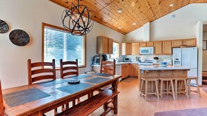 Una cocina amplia con armarios de madera, una isla central con taburetes y una zona de comedor con mesa y bancos de madera.