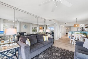 Ein modernes Wohnzimmer mit einem grauen Sofa, einem Essbereich mit einem weißen Tisch und einer Küche im Hintergrund.