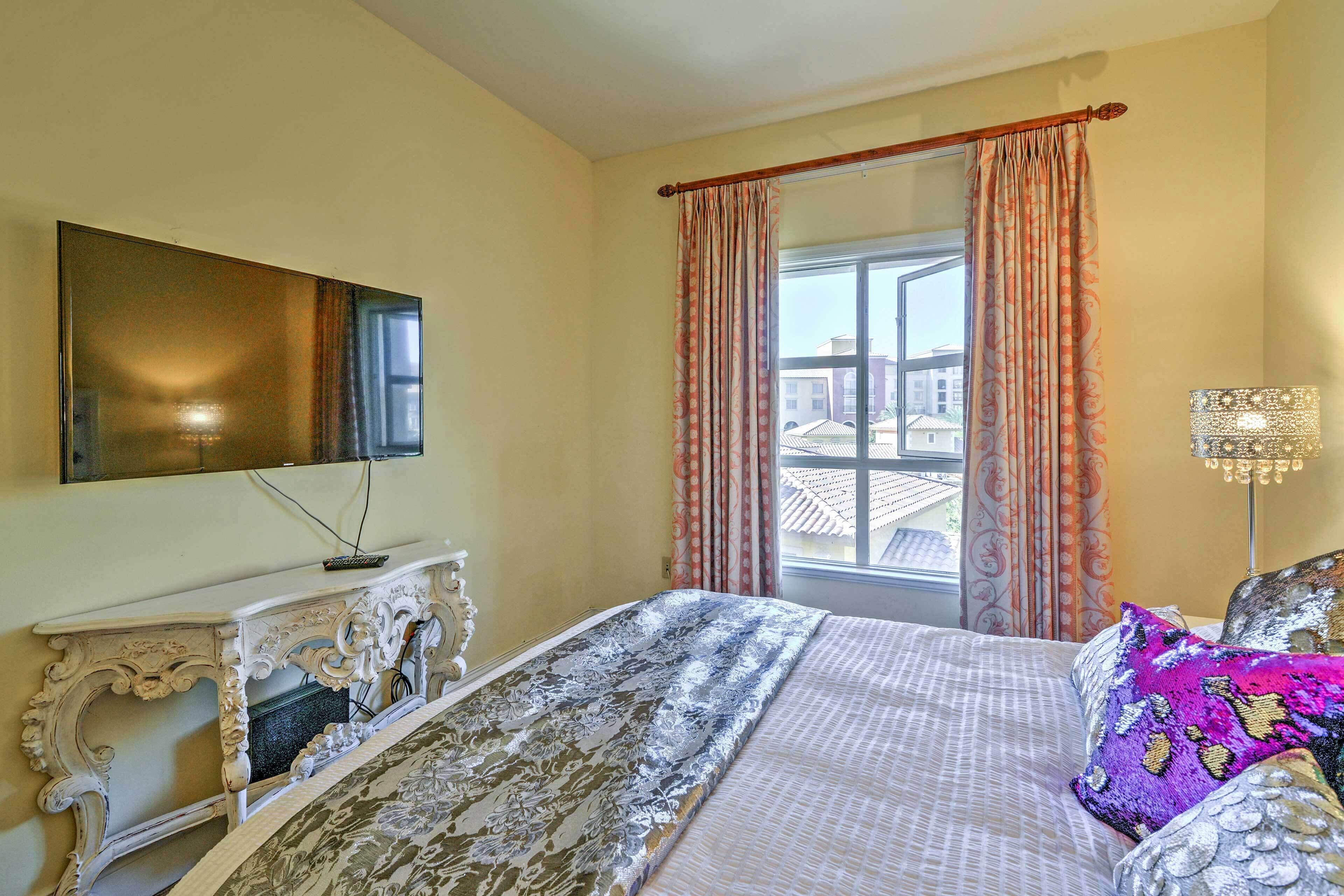 A hotel room with a bed, a television on a stand, a window with curtains, and a lamp.