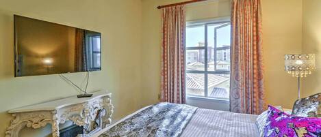 A hotel room with a bed, a television on a stand, a window with curtains, and a lamp.