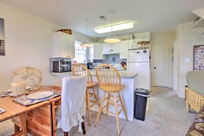 A compact kitchen with white cabinets, a refrigerator, and a microwave. There is a dining area with a table set for two, two wooden chairs, and a candle. - < 1 Mi to Beach! Waterfront Galveston Bay Retreat (Galveston)