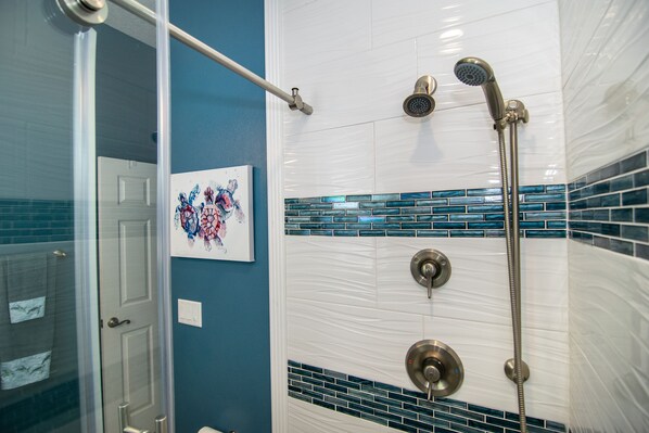 A bathroom with a glass shower enclosure, a white tiled wall with blue mosaic tiles, and a door with a towel rack.
