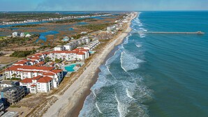 An aerial view of a coastal residential area with beachfront properties, a pier extending into the ocean, and a large swimming pool. - Soak Up the Sun at 312-A Villa Capriani! (North Topsail Beach)