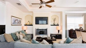 A living room with a grey sofa, a fireplace, a ceiling fan, and a dining area with a table and chairs. - Lively Home with Water Views at Reunion (Kissimmee)