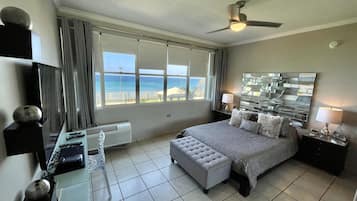 A hotel room with a bed, a desk with a computer, a TV, and a view of the ocean.