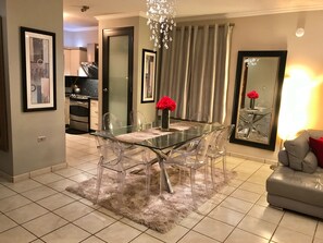 A modern dining area with a glass table and chairs, a fluffy rug, and a chandelier.