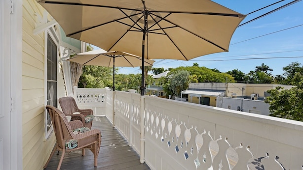 A balcony with wicker chairs and a large umbrella, overlooking a residential area with houses and trees. - **SUZY'S PARROT PERCH @ OLD TOWN** Condo + Last Key White Glove Service... (Key West)