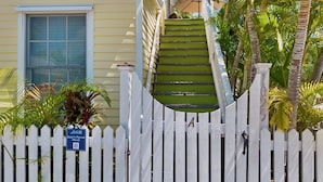 A white picket fence with a sign reading "Suzy's Parrot Perch" and a number "102" on a building. - **SUZY'S PARROT PERCH @ OLD TOWN** Condo + Last Key White Glove Service... (Key West)