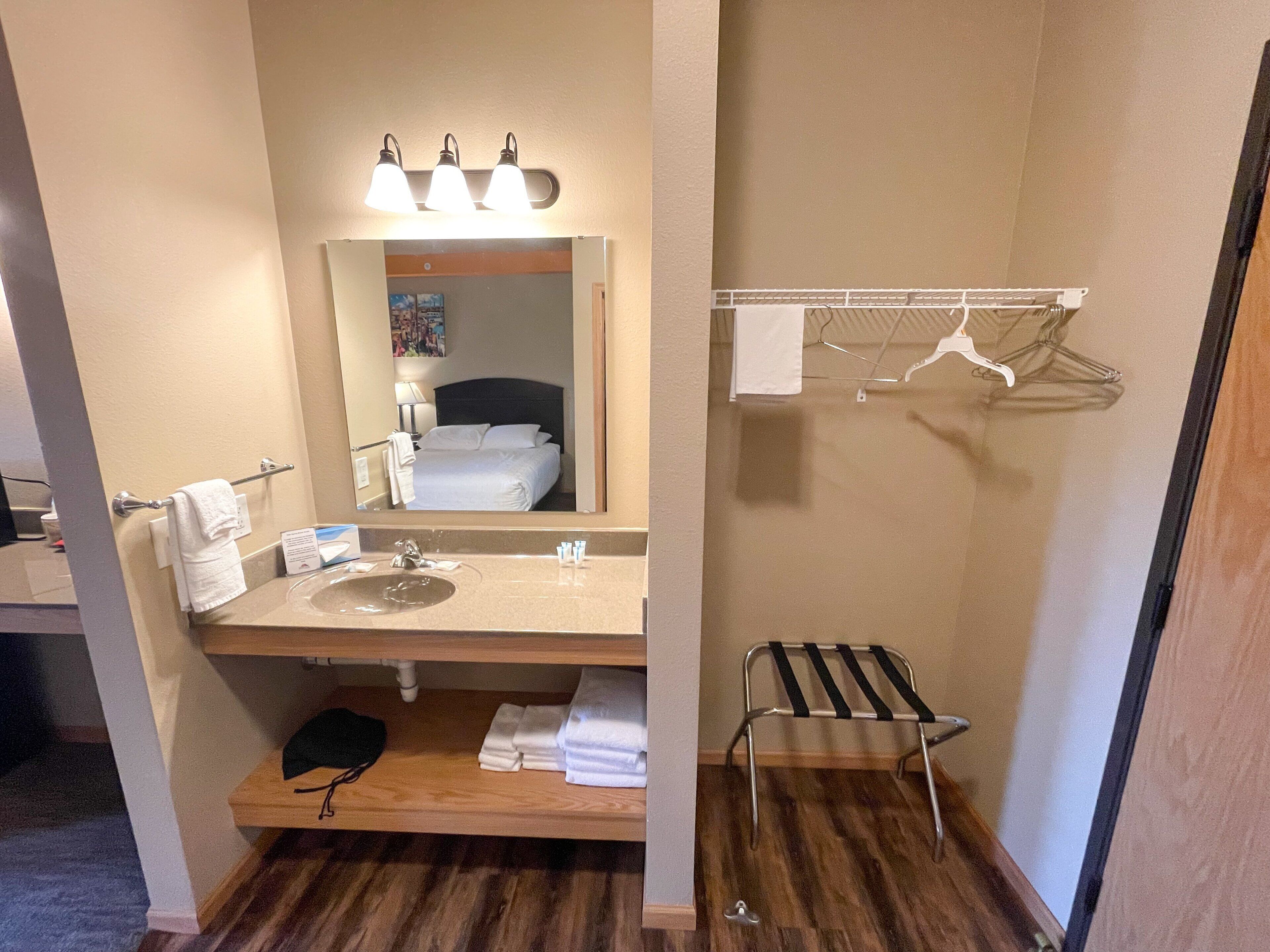 A hotel bathroom with a sink, mirror, towel rack, and a small shelf with folded towels.
