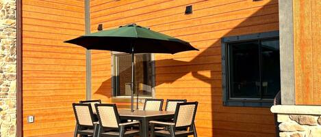 An outdoor patio with a table and chairs, a green umbrella, and a stone wall.