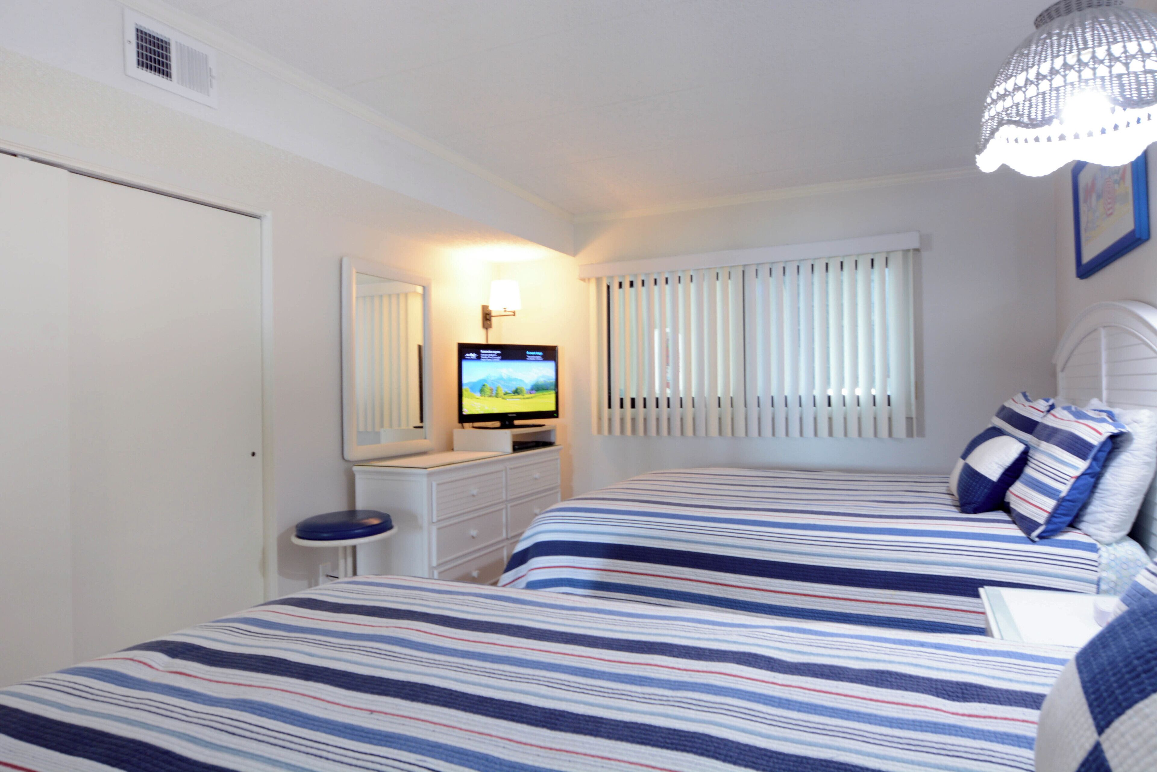Un dormitorio con dos camas, televisor, cómoda y ventana con persianas.