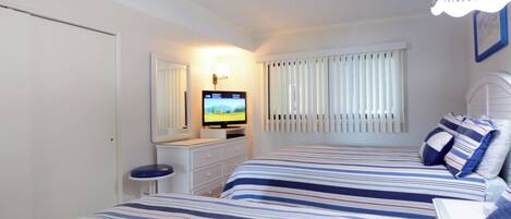 Un dormitorio con dos camas, televisor, cómoda y ventana con persianas.
