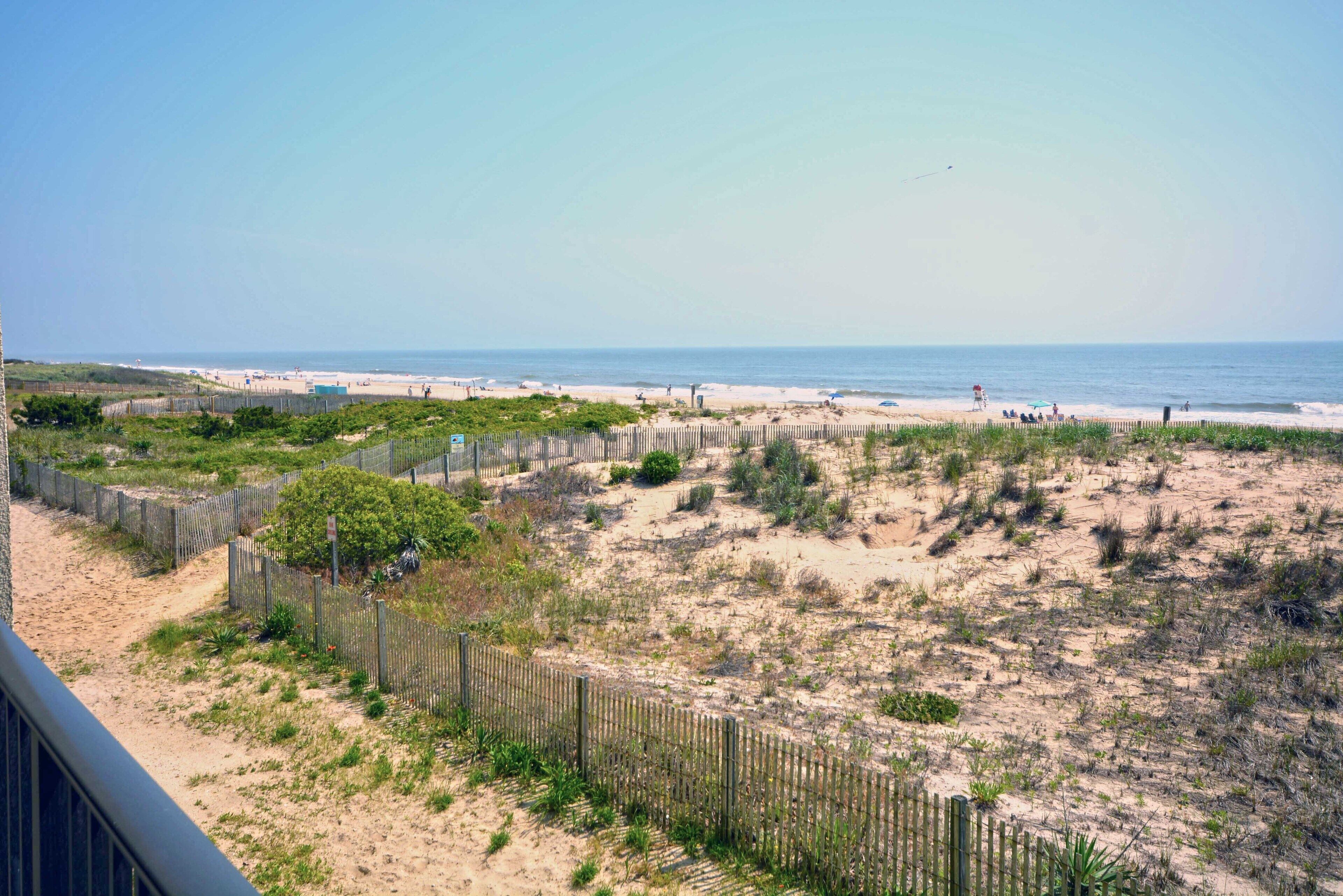A beach view with a wooden fence, sandy dunes, and a lifeguard tower.