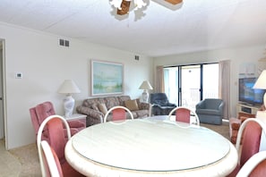 A living room with a round table, two sofas, a television, and a painting on the wall. - Cozy, comfortable 2 bedroom oceanfront condo with coastal decor, free WiFi, and gorgeous view of the ocean and dunes just steps to the beach! (Ocean City)