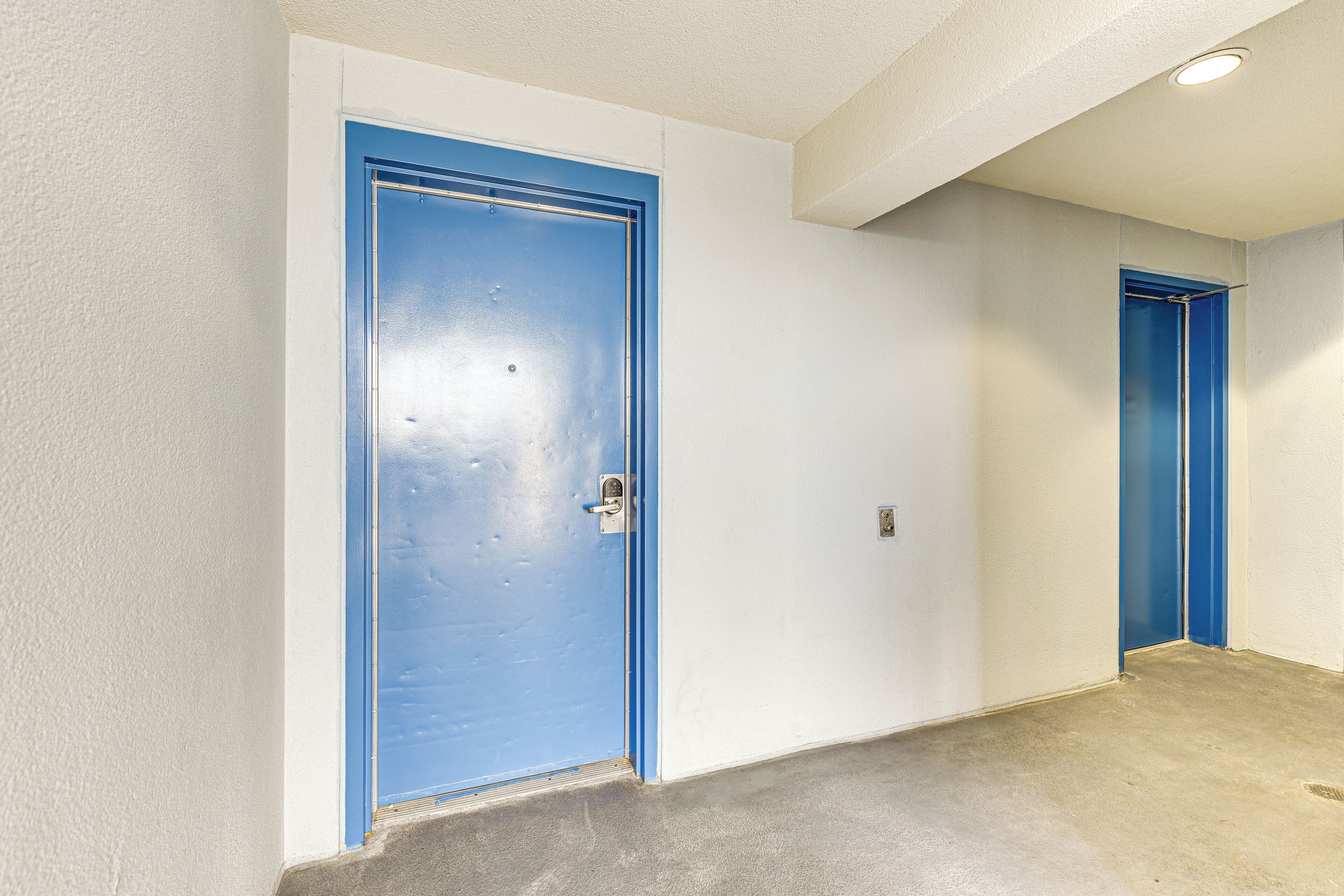 Un couloir avec deux portes bleues, des murs blancs et un sol en béton.