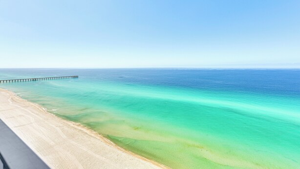 Une plage bordée d’une eau turquoise et cristalline, avec une longue jetée qui s’avance dans la mer.