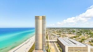 Un grand hôtel avec vue sur la plage, un parking et une ville côtière en arrière-plan.