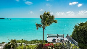 Vista de una playa tropical con una terraza de madera y sillones de descanso frente a aguas turquesas.