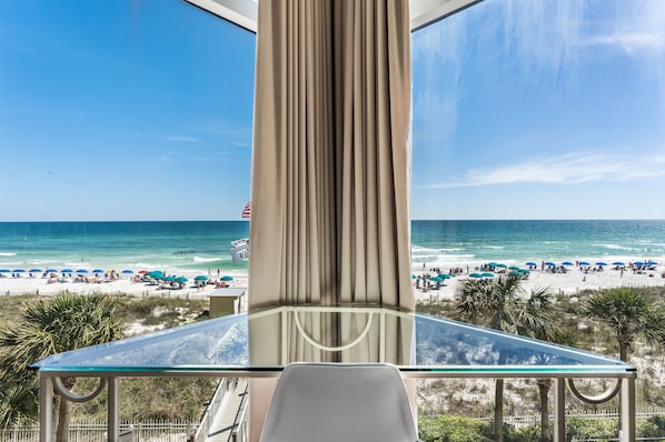 Enjoy the ocean views from this beachfront balcony with a glass table and comfortable chair.