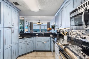 Enjoy cooking in this well-lit kitchen with a large window overlooking a scenic view, featuring a stainless steel range hood and black countertop.