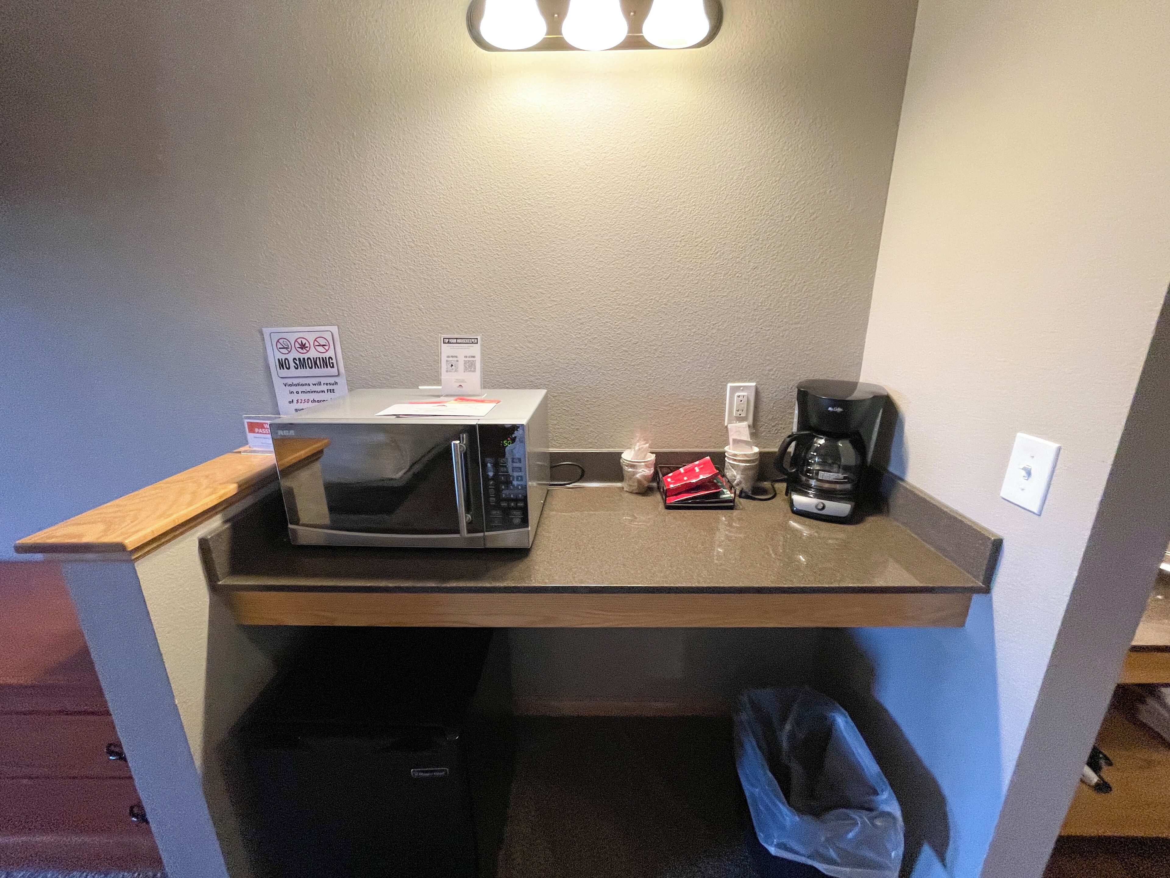 A kitchenette with a microwave, coffee maker, and a trash bin.