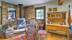 Un interior rústico con una chimenea de ladrillo, una mesa de madera, una silla de mimbre y una estantería.