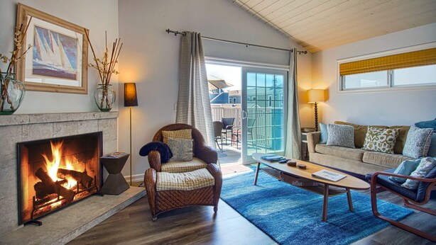 A cozy living room with a fireplace, a comfortable sofa, a coffee table, and a view of the outdoors through a sliding glass door. - Beautiful newly remodeled upper unit located within the first block to beach! (Newport Beach)