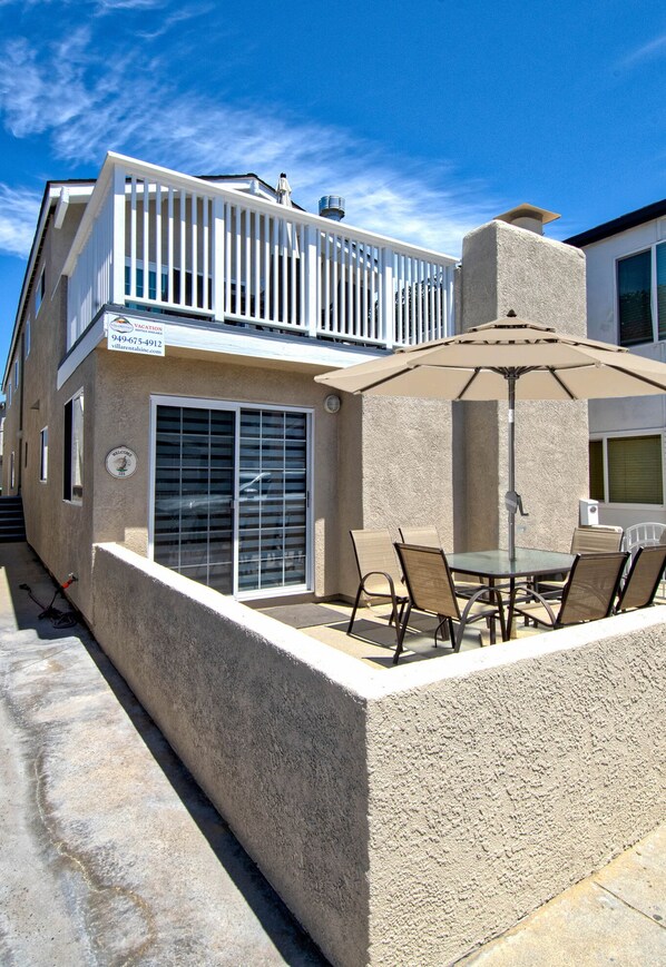 A two-story house with a balcony, a patio with a table and chairs, and a large umbrella.