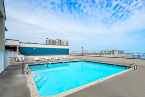 Ein Dachpool mit klarem, blauem Wasser, umgeben von Liegestühlen und einem weißen Zaun.