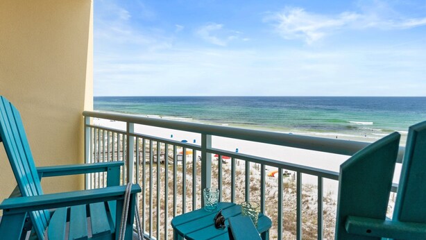 Un balcon avec deux fauteuils Adirondack verts, une petite table et une vue sur la plage et l’océan.