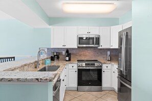 A modern kitchen with white cabinets, a built-in microwave, a stainless steel refrigerator, a coffee maker, and a dishwasher.