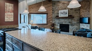A kitchen with granite countertops, a stone fireplace, and a large island. - Ski-In Condo Featuring Vaulted Ceilings, On-Site Hot Tubs, Private Patios, Cover (Breckenridge)
