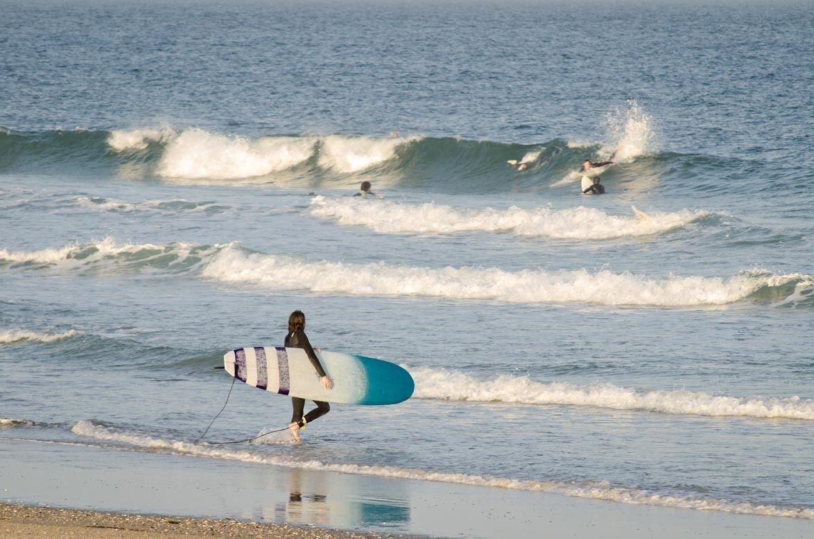 A beach with waves and a surfer walking with a surfboard.