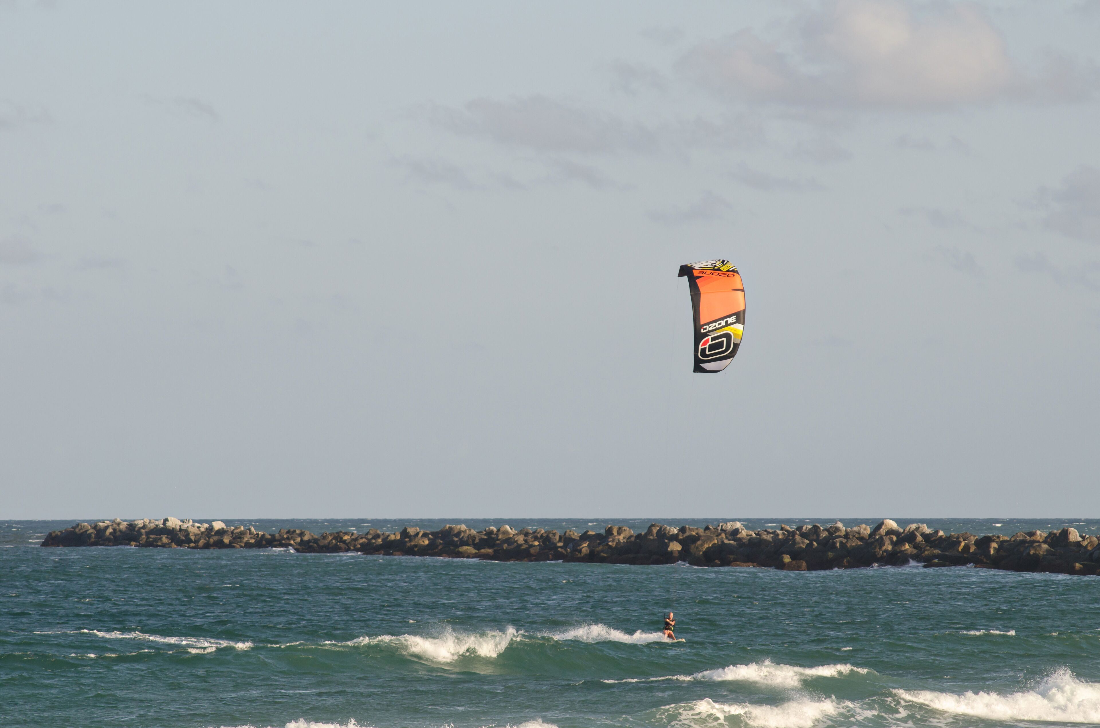 A person kiteboarding over a rocky shoreline with waves.