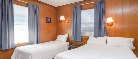 Une chambre avec deux lits simples, des murs en bois, un ventilateur de plafond et deux lampes fixées au mur.