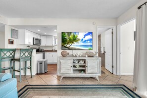 A modern living room with a flat-screen TV, a kitchen area, and a dining space.