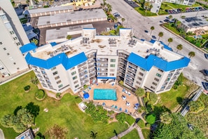 A multi-story hotel with a rooftop pool, surrounded by greenery and a parking area.