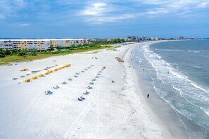 A beach with rows of umbrellas and a hotel in the background.