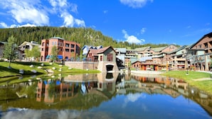 A lakeside resort with a central bridge, reflecting buildings, and a mountainous backdrop.