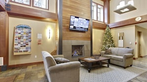 A spacious lobby with a fireplace, comfortable seating, a Christmas tree, and a mounted TV.