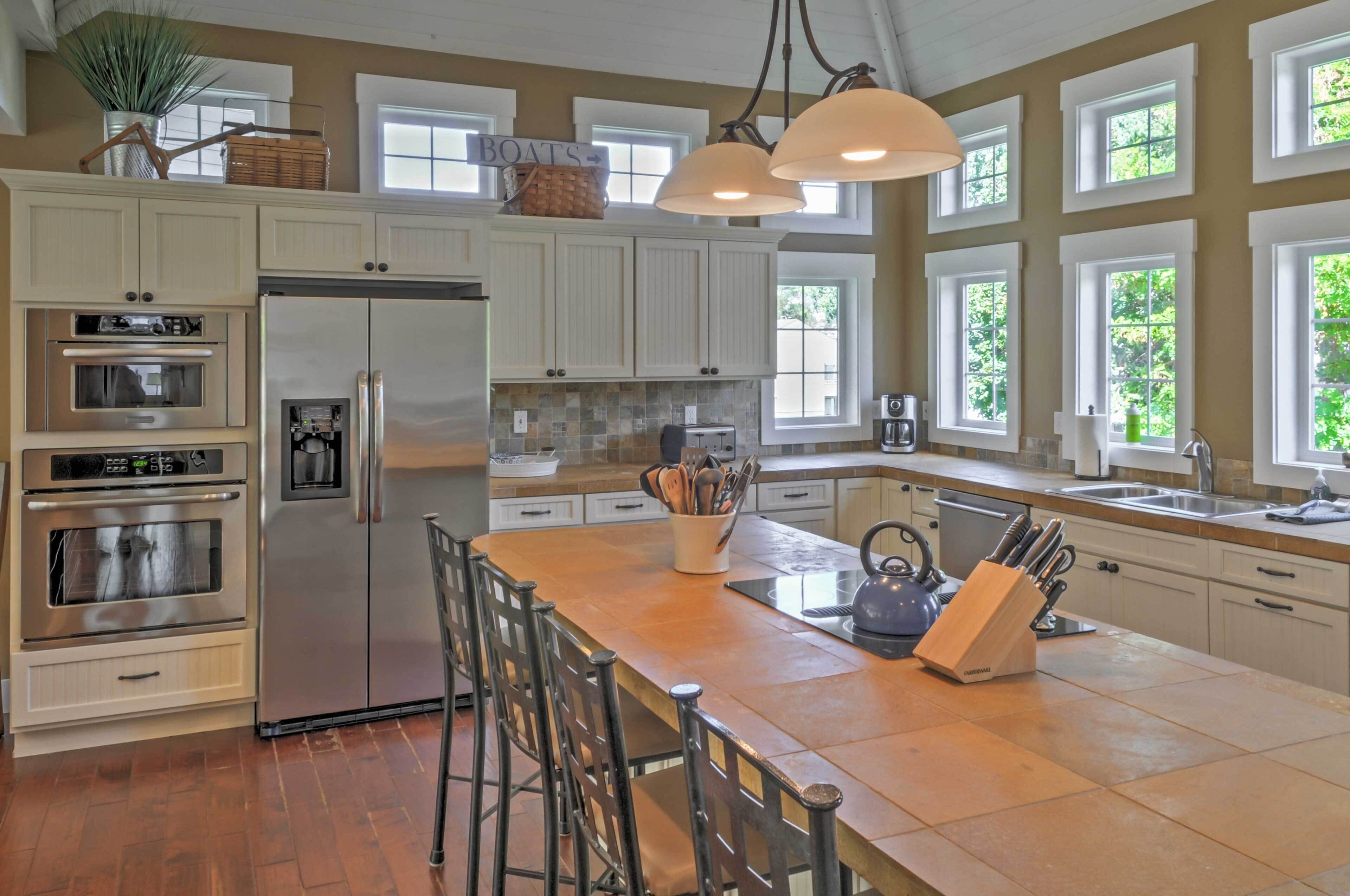 A spacious kitchen with white cabinetry, stainless steel appliances, a large island with bar stools, and multiple windows providing natural light.
