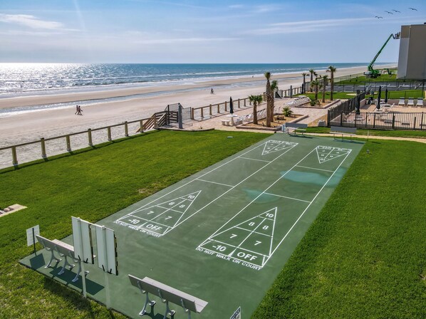 A green shuffleboard court with a view of the beach and ocean.